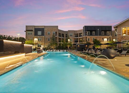 A large swimming pool in front of a building with lights on the side.