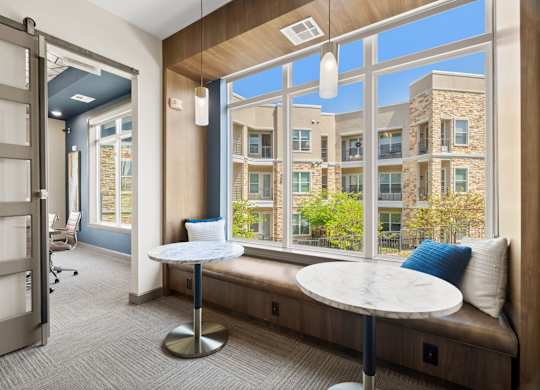 A room with a table and a bench with a view of a building outside.