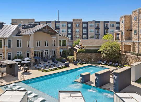 A large swimming pool surrounded by lounge chairs and umbrellas in front of a building.