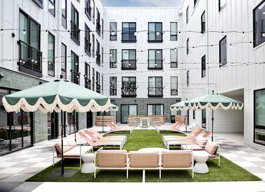 A patio with white furniture and green umbrellas is surrounded by white buildings.