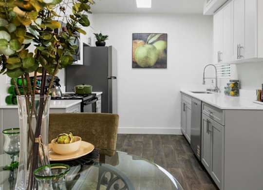 A modern kitchen with a glass table and a bowl of fruit on it.