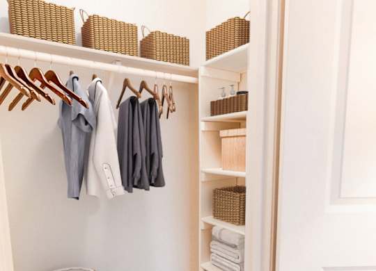 A white closet with clothes hanging and shelves with baskets.