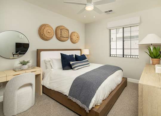 A bedroom with a bed, desk, chair, and a mirror.