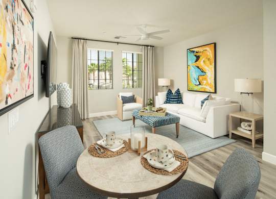 A living room with a grey sofa, a round table with two chairs and a painting on the wall.