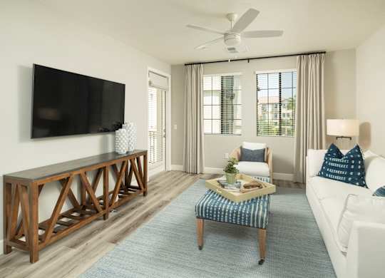 A living room with a white couch, a wooden coffee table, and a flat-screen TV mounted on the wall.