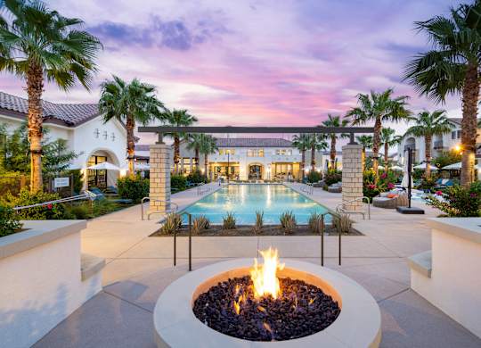A fire pit sits in the middle of a patio surrounded by palm trees.