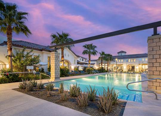 A pool surrounded by palm trees and a building in the background.