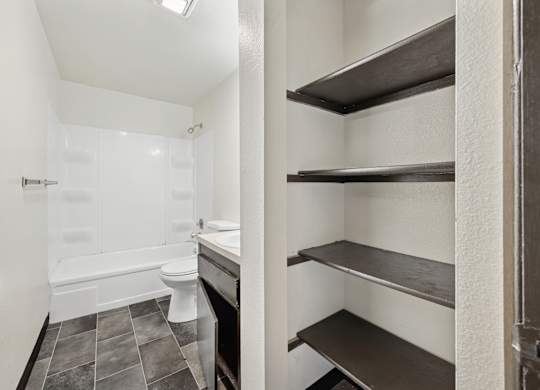 A white bathroom with a toilet, sink, and shelves.