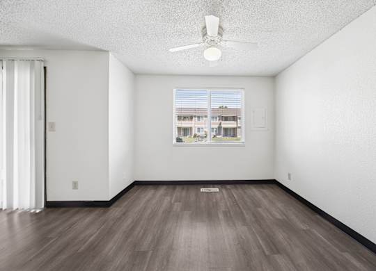 A room with a ceiling fan and a window showing a building outside.