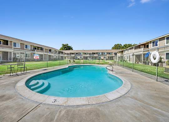 A round swimming pool in the middle of a concrete area with a fence and chairs around it.