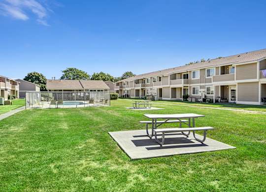 A picnic table sits in the middle of a grassy area in front of apartment buildings.