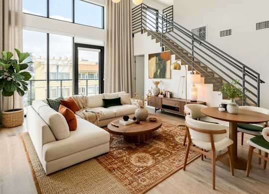 A living room with a staircase, a sofa, a table, and chairs.