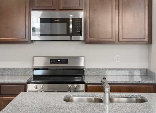 A modern kitchen with a stainless steel oven and microwave above a granite countertop.