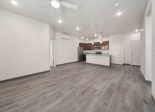 A spacious room with wooden flooring and a kitchen area in the background.