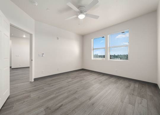 A room with a ceiling fan and two windows.