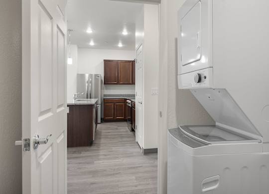 A white door is open to a kitchen with a refrigerator and oven.