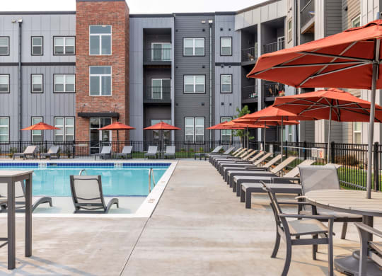 a swimming pool with chairs and umbrellas in front of an apartment building