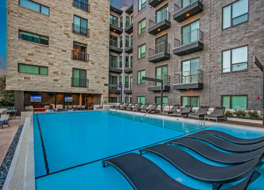 a swimming pool with chaise lounge chairs in front of an apartment building