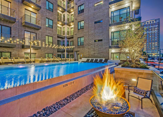a pool with a fire pit and lounge chairs in front of an apartment building