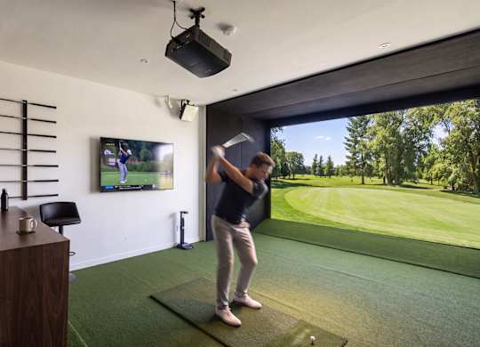 A man is playing golf in a room with a large screen showing a golf course.
