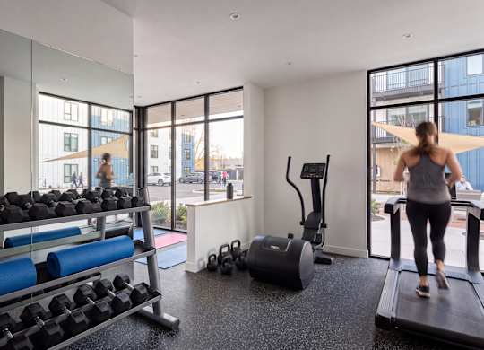 A woman is working out on a treadmill in a spacious gym with a view of the city.