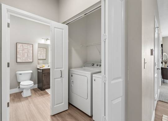 A white bathroom with a toilet, sink, and washer and dryer.