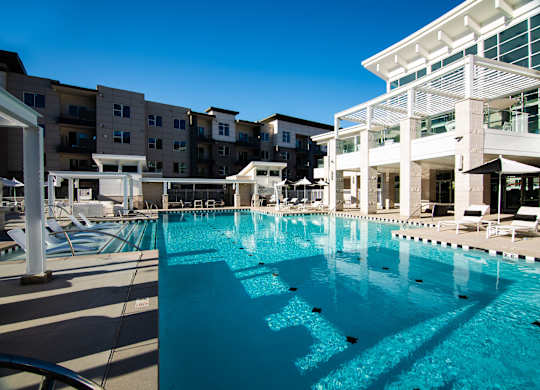 A large swimming pool in front of a building with sun loungers.