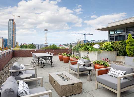 A patio with grey couches and a table with a fire pit in the middle.