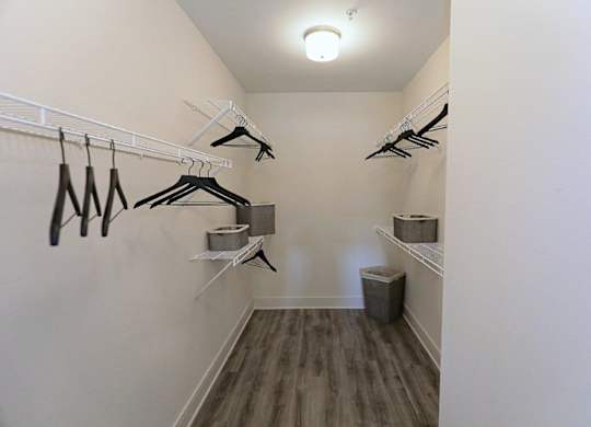 A walk in closet with clothes hanging and a trash can.