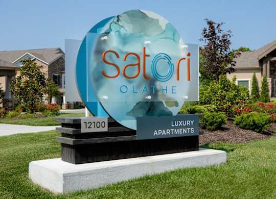 A sign for Satori Olai Luxury Apartments is displayed in front of some houses.