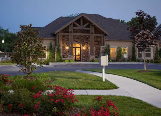A house with a stone facade and a large front yard with red flowers.