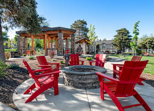 A fire pit surrounded by red chairs in a backyard setting.