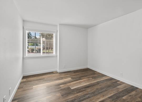A room with wooden flooring and a window with blinds.