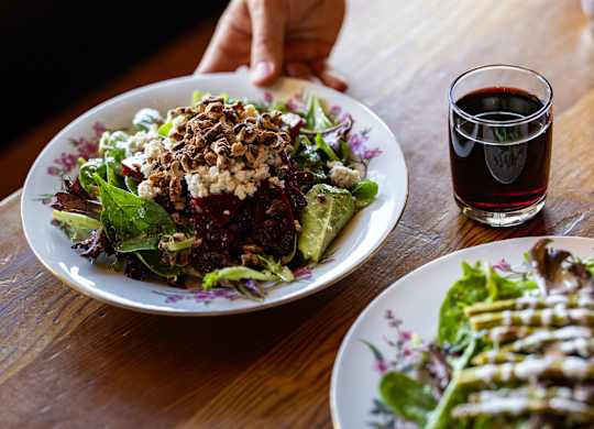 A person is sitting at a table with a plate of salad and a glass of red wine.