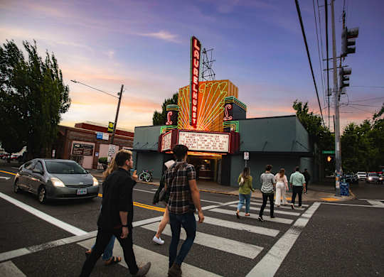 A group of people are crossing the street in front of a brightly lit theater.