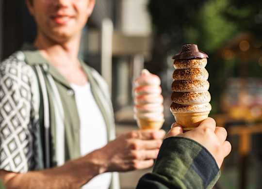 A man holding two ice cream cones with one having a chocolate topping.