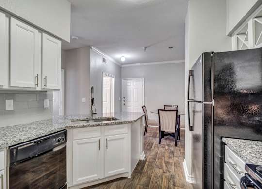 A kitchen with a black refrigerator, white cabinets, and a granite countertop.