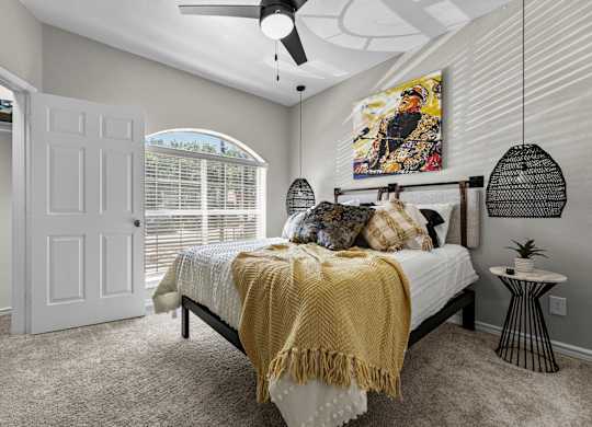 A bedroom with a bed, a ceiling fan, and a painting on the wall.