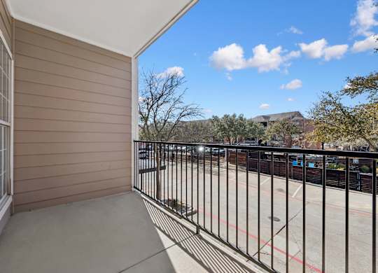 A balcony with a black railing and a view of a parking lot and trees.