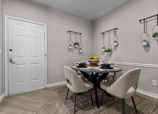 A dining room with a white door, a round table with four chairs, and three hanging planters.