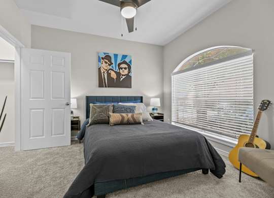 A bedroom with a bed, a ceiling fan, and a guitar.