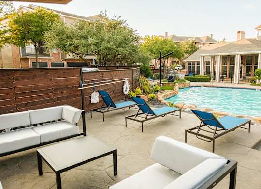 A poolside patio with a white couch and blue chairs.