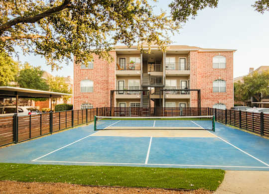 A tennis court is located in front of a red brick building.