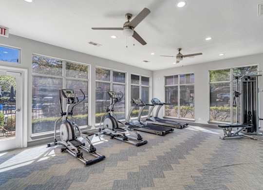 A gym with treadmills, exercise bikes, and a ceiling fan.