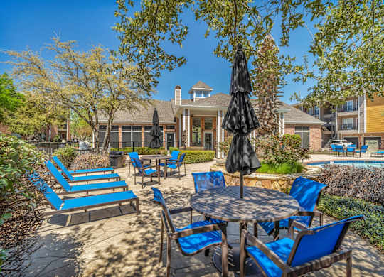 A patio with blue chairs and a table with a black umbrella.