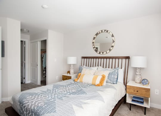 A bedroom with a bed, two lamps, and a mirror on the wall.
