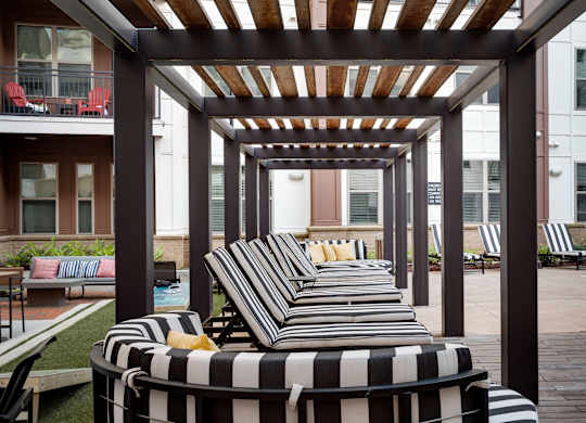an outdoor lounge area with striped lounge chairs and a pergola