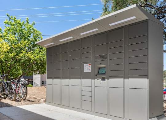 A grey utility box with a small window and a door is situated on a sidewalk.