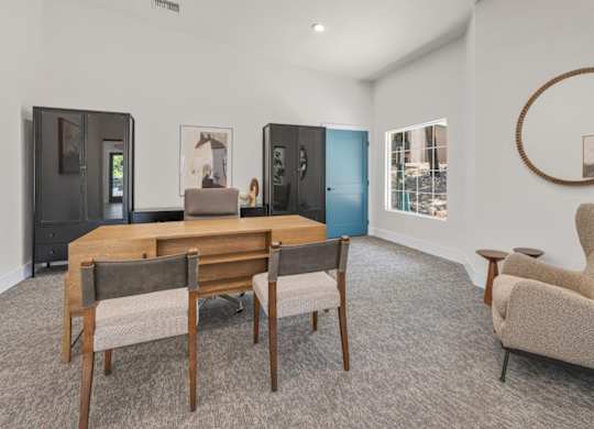A room with a wooden table and chairs, a round mirror, and a framed picture on the wall.