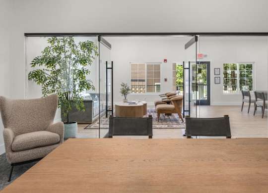 A room with a wooden table and chairs in the foreground and a glass wall in the background.